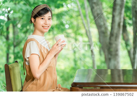 一位女顧客在一家可以俯瞰鬱鬱蔥蔥的森林的咖啡館裡喝飲料。 一位女顧客在一家可以俯瞰鬱鬱蔥蔥的森林的咖啡館裡喝飲料。 139867502