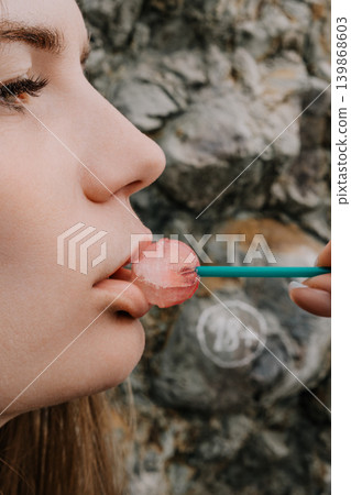 Lollipop Woman Candy Profile view of a young woman eating a sweet pink treat outdoors against a natural rocky wall background Lollipop Woman Candy Profile view of a young woman eating a sweet pink treat outdoors against a natural rocky wall background 139868603