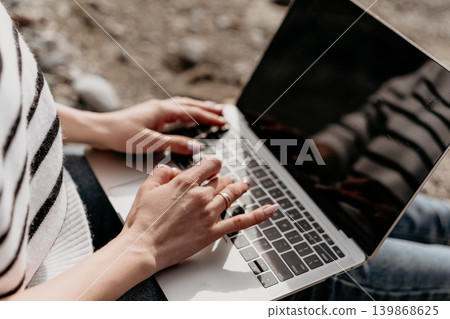 Typing laptop freelance worker sitting on a coastal beach using a portable computer for remote work during a sunny day 139868625