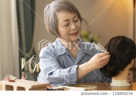 一位老婦人用水引繩製作髮飾,並將其插入人體模型中。 一位老婦人用水引繩製作髮飾,並將其插入人體模型中。 139869254