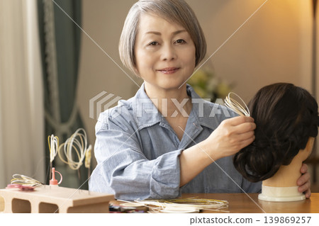 一位老婦人用水引繩製作髮飾,並將其插入人體模型中。 一位老婦人用水引繩製作髮飾,並將其插入人體模型中。 139869257