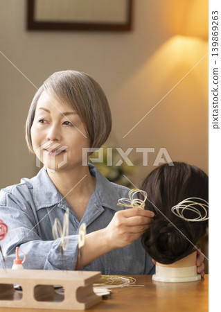 一位老婦人用水引繩製作髮飾,並將其插入人體模型中。 一位老婦人用水引繩製作髮飾,並將其插入人體模型中。 139869263