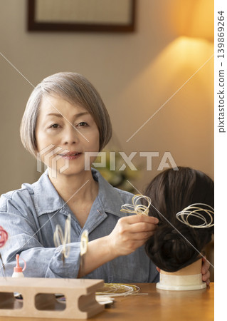 一位老婦人用水引繩製作髮飾，並將其插入人體模型中。 139869264