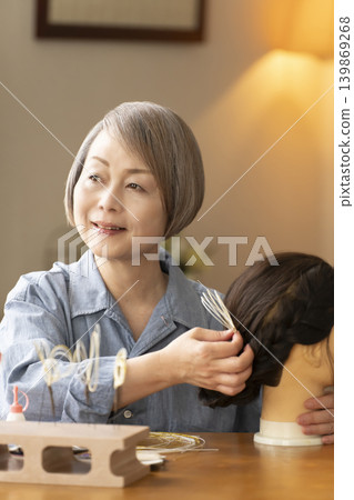A senior woman makes a hair ornament using mizuhiki (decorative cord) and inserts it into a mannequin. A senior woman makes a hair ornament using mizuhiki (decorative cord) and inserts it into a mannequin. 139869268