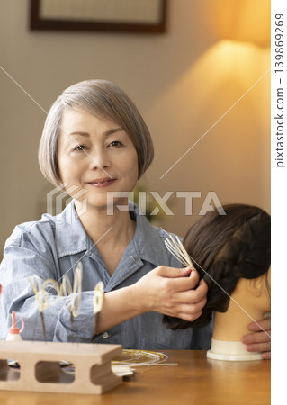 一位老婦人用水引繩製作髮飾，並將其插入人體模型中。 139869269