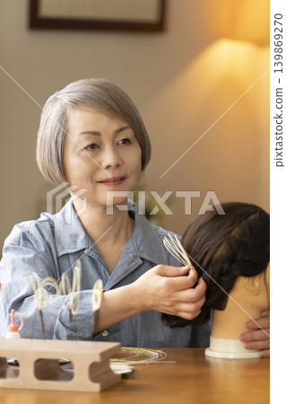 一位老婦人用水引繩製作髮飾,並將其插入人體模型中。 一位老婦人用水引繩製作髮飾,並將其插入人體模型中。 139869270