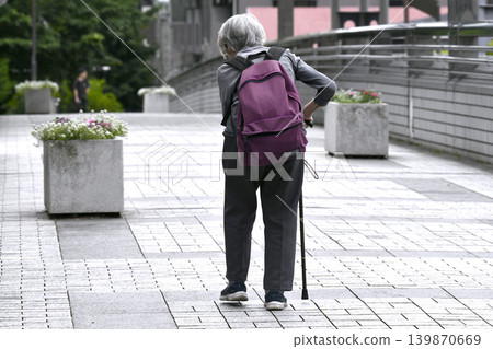 A cityscape of Yokohama, Japan: An elderly woman with a bent back and a cane, carrying a backpack... She has difficulty using the stairs of a pedestrian overpass and has to take a detour. A cityscape of Yokohama, Japan: An elderly woman with a bent back and a cane, carrying a backpack... She has difficulty using the stairs of a pedestrian overpass and has to take a detour. 139870669