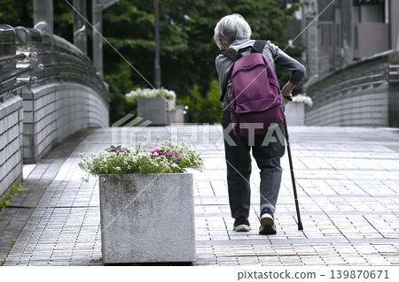 日本橫濱市的城市景觀：一位駝背的老婦人拄著拐杖，背著背包……她上下人行天橋的樓梯很困難，不得不繞道而行。 139870671