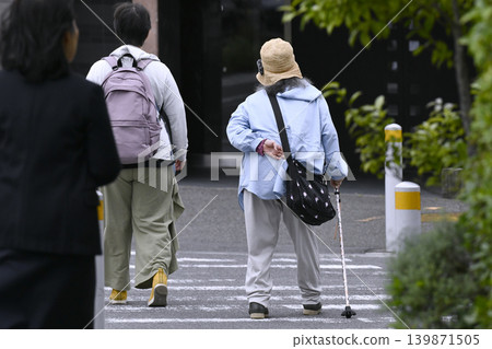 A street scene in Yokohama, Japan: An elderly woman with a cane and a bent back crosses the street... accompanied by a kind-looking woman to her left. (Yokohama City) A street scene in Yokohama, Japan: An elderly woman with a cane and a bent back crosses the street... accompanied by a kind-looking woman to her left. (Yokohama City) 139871505