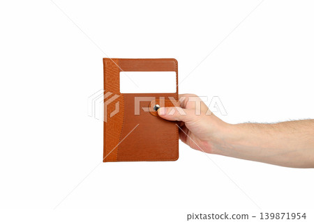 male hand holding a closed brown notebook isolated on a white background male hand holding a closed brown notebook isolated on a white background 139871954