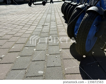 Electric scooters lined up on brick pavement under sunlight in urban area, suitable as background Electric scooters lined up on brick pavement under sunlight in urban area, suitable as background 139872563