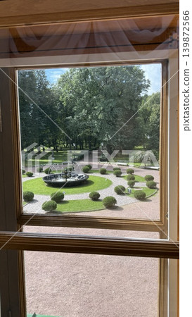 View from window overlooking elegant garden with fountain and manicured hedges on sunny day View from window overlooking elegant garden with fountain and manicured hedges on sunny day 139872566