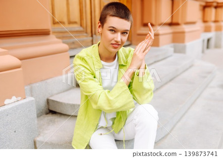 Stylish young woman with short haircut posing on city streets. The concept of fashion, style. Stylish young woman with short haircut posing on city streets. The concept of fashion, style. 139873741