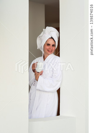 A woman in a robe and towel drinks a hot drink on a terrace after a shower 139874016