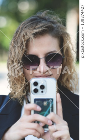 Caucasian woman with curly hair using her mobile phone outdoors. Close-up. Communication technology and modern lifestyle concept Caucasian woman with curly hair using her mobile phone outdoors. Close-up. Communication technology and modern lifestyle concept 139874427