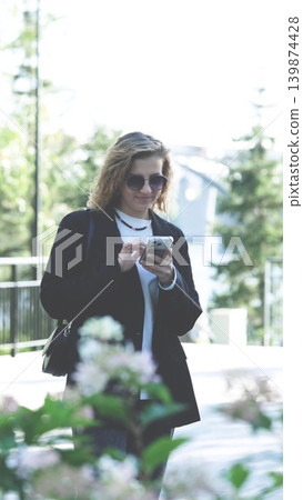 Caucasian woman with curly hair using her mobile phone outdoors. Close-up. Communication technology and modern lifestyle concept Caucasian woman with curly hair using her mobile phone outdoors. Close-up. Communication technology and modern lifestyle concept 139874428