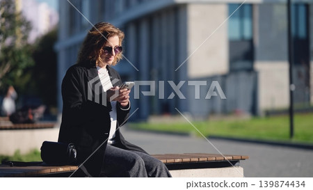 Caucasian woman with curly hair using her mobile phone outdoors. Close-up. Communication technology and modern lifestyle concept Caucasian woman with curly hair using her mobile phone outdoors. Close-up. Communication technology and modern lifestyle concept 139874434