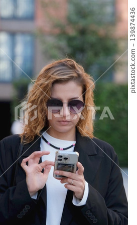 Caucasian woman with curly hair using her mobile phone outdoors. Close-up. Communication technology and modern lifestyle concept Caucasian woman with curly hair using her mobile phone outdoors. Close-up. Communication technology and modern lifestyle concept 139874436