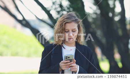 Caucasian woman with curly hair using her mobile phone outdoors. Close-up. Communication technology and modern lifestyle concept Caucasian woman with curly hair using her mobile phone outdoors. Close-up. Communication technology and modern lifestyle concept 139874451