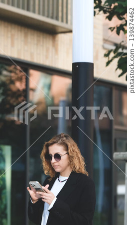 Caucasian woman with curly hair using her mobile phone outdoors. Close-up. Communication technology and modern lifestyle concept 139874462