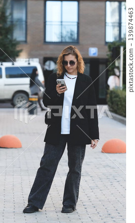 Caucasian woman with curly hair using her mobile phone outdoors. Close-up. Communication technology and modern lifestyle concept 139874463