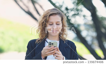 Caucasian woman with curly hair using her mobile phone outdoors. Close-up. Communication technology and modern lifestyle concept Caucasian woman with curly hair using her mobile phone outdoors. Close-up. Communication technology and modern lifestyle concept 139874486
