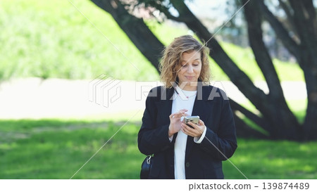 Caucasian woman with curly hair using her mobile phone outdoors. Close-up. Communication technology and modern lifestyle concept 139874489