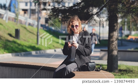 Caucasian woman with curly hair using her mobile phone outdoors. Close-up. Communication technology and modern lifestyle concept 139874493