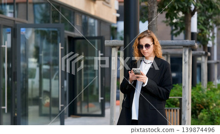 Caucasian woman with curly hair using her mobile phone outdoors. Close-up. Communication technology and modern lifestyle concept Caucasian woman with curly hair using her mobile phone outdoors. Close-up. Communication technology and modern lifestyle concept 139874496