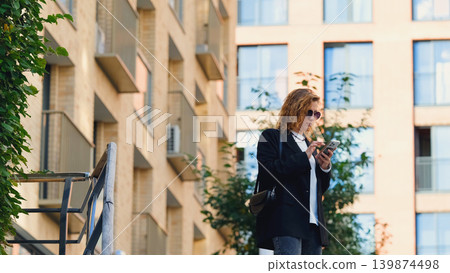 Caucasian woman with curly hair using her mobile phone outdoors. Close-up. Communication technology and modern lifestyle concept Caucasian woman with curly hair using her mobile phone outdoors. Close-up. Communication technology and modern lifestyle concept 139874498