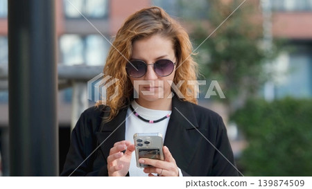 Caucasian woman with curly hair using her mobile phone outdoors. Close-up. Communication technology and modern lifestyle concept Caucasian woman with curly hair using her mobile phone outdoors. Close-up. Communication technology and modern lifestyle concept 139874509