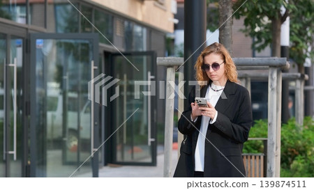 Caucasian woman with curly hair using her mobile phone outdoors. Close-up. Communication technology and modern lifestyle concept Caucasian woman with curly hair using her mobile phone outdoors. Close-up. Communication technology and modern lifestyle concept 139874511