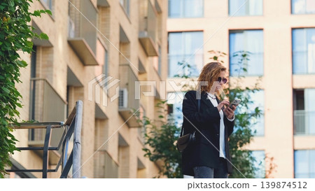 Caucasian woman with curly hair using her mobile phone outdoors. Close-up. Communication technology and modern lifestyle concept Caucasian woman with curly hair using her mobile phone outdoors. Close-up. Communication technology and modern lifestyle concept 139874512