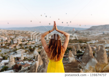 Woman stands on mountain with flying air balloons on background. Tourist Turkish region Cappadocia. 139874737
