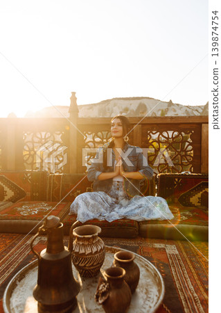 Young woman meditates on terrace with stunning city views in Cappadocia. Concept of active lifestyle Young woman meditates on terrace with stunning city views in Cappadocia. Concept of active lifestyle 139874754