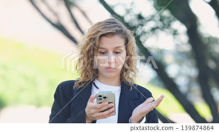 Caucasian woman with curly hair using her mobile phone outdoors. Close-up. Communication technology and modern lifestyle concept Caucasian woman with curly hair using her mobile phone outdoors. Close-up. Communication technology and modern lifestyle concept 139874864