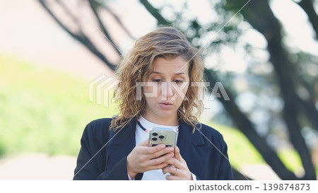 Caucasian woman with curly hair using her mobile phone outdoors. Close-up. Communication technology and modern lifestyle concept Caucasian woman with curly hair using her mobile phone outdoors. Close-up. Communication technology and modern lifestyle concept 139874873