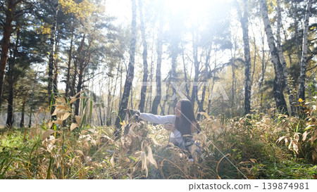 A cute young woman with a dog enjoys the beauty of nature and communication with pets. The woman drinks tea from a thermos during a picnic in the autumn forest 139874981