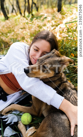 Young woman relaxes while walking her dog in autumn forest Young woman relaxes while walking her dog in autumn forest 139875046