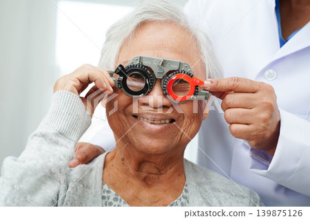 Optometrist checking Asian elderly woman ophthalmic vision eye test and using optical trial frame. 139875126