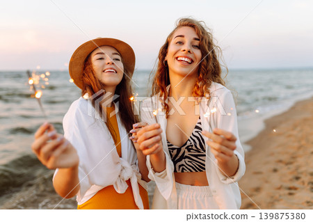 The sparklers in the hands of young women on the beach. Happy women walking with sparkler fireworks The sparklers in the hands of young women on the beach. Happy women walking with sparkler fireworks 139875380