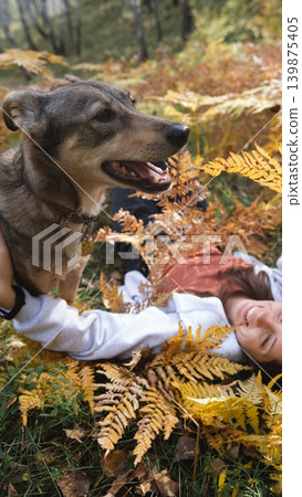Young woman relaxes while walking her dog in autumn forest Young woman relaxes while walking her dog in autumn forest 139875405