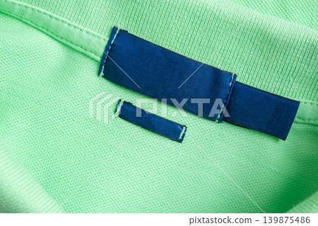 Blank blue laundry care clothes label on green shirt fabric texture background Blank blue laundry care clothes label on green shirt fabric texture background 139875486