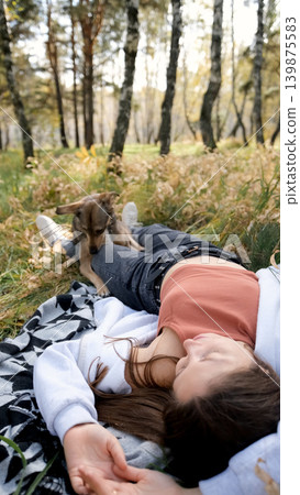 Young woman relaxes while walking her dog in autumn forest Young woman relaxes while walking her dog in autumn forest 139875583