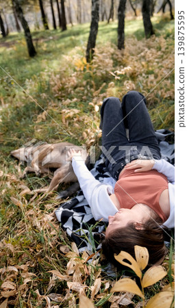 Young woman relaxes while walking her dog in autumn forest 139875595