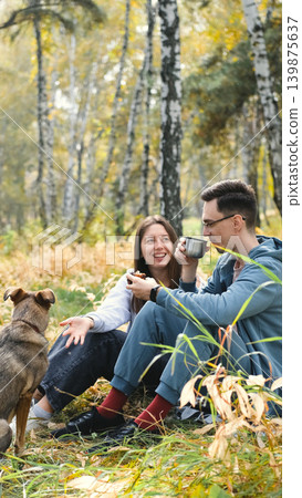 A woman and a man in love are walking in an autumn forest, in tall yellow grass, in fern leaves, a dog is walking next to them. A married couple is relaxing in nature during a walk with their beloved A woman and a man in love are walking in an autumn forest, in tall yellow grass, in fern leaves, a dog is walking next to them. A married couple is relaxing in nature during a walk with their beloved 139875637
