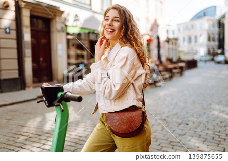 Happy woman rides electric scooter at weekend leisure time. Ecological transport. Active lifestyle. Happy woman rides electric scooter at weekend leisure time. Ecological transport. Active lifestyle. 139875655