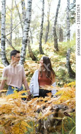 Married couple relaxing in nature during a walk in the autumn forest. Woman and man in love walking through tall yellow grass, in fern leaves Married couple relaxing in nature during a walk in the autumn forest. Woman and man in love walking through tall yellow grass, in fern leaves 139875674