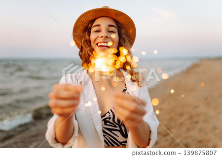 The sparklers in the hands of young woman on the beach. Summer holidays and lifestyle concept. The sparklers in the hands of young woman on the beach. Summer holidays and lifestyle concept. 139875807