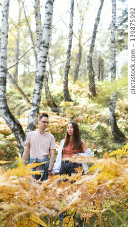 Married couple relaxing in nature during a walk in the autumn forest. Woman and man in love walking through tall yellow grass, in fern leaves 139875992